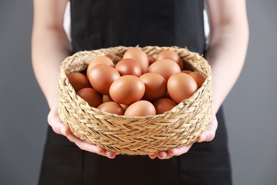 Photo of Woman with basket of eggs on grey background, closeup