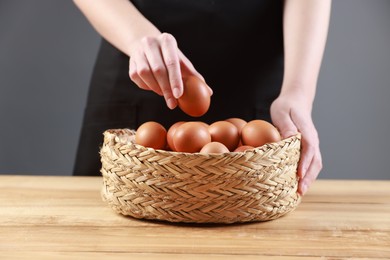 Photo of Woman with basket of eggs at wooden table on grey background, closeup