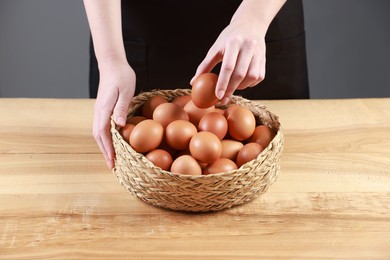 Photo of Woman with basket of eggs at wooden table on grey background, closeup