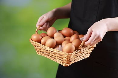 Photo of Woman with basket of eggs on blurred background, closeup