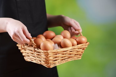 Photo of Woman with basket of eggs on blurred background, closeup