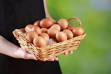 Photo of Woman with basket of eggs on blurred background, closeup