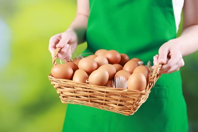 Photo of Woman with basket of eggs on blurred background, closeup