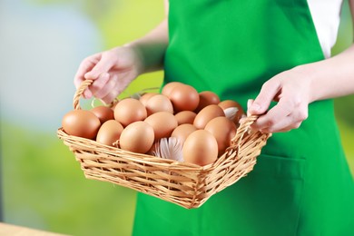 Photo of Woman with basket of eggs on blurred background, closeup