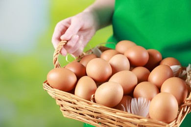 Photo of Woman with basket of eggs on blurred background, closeup