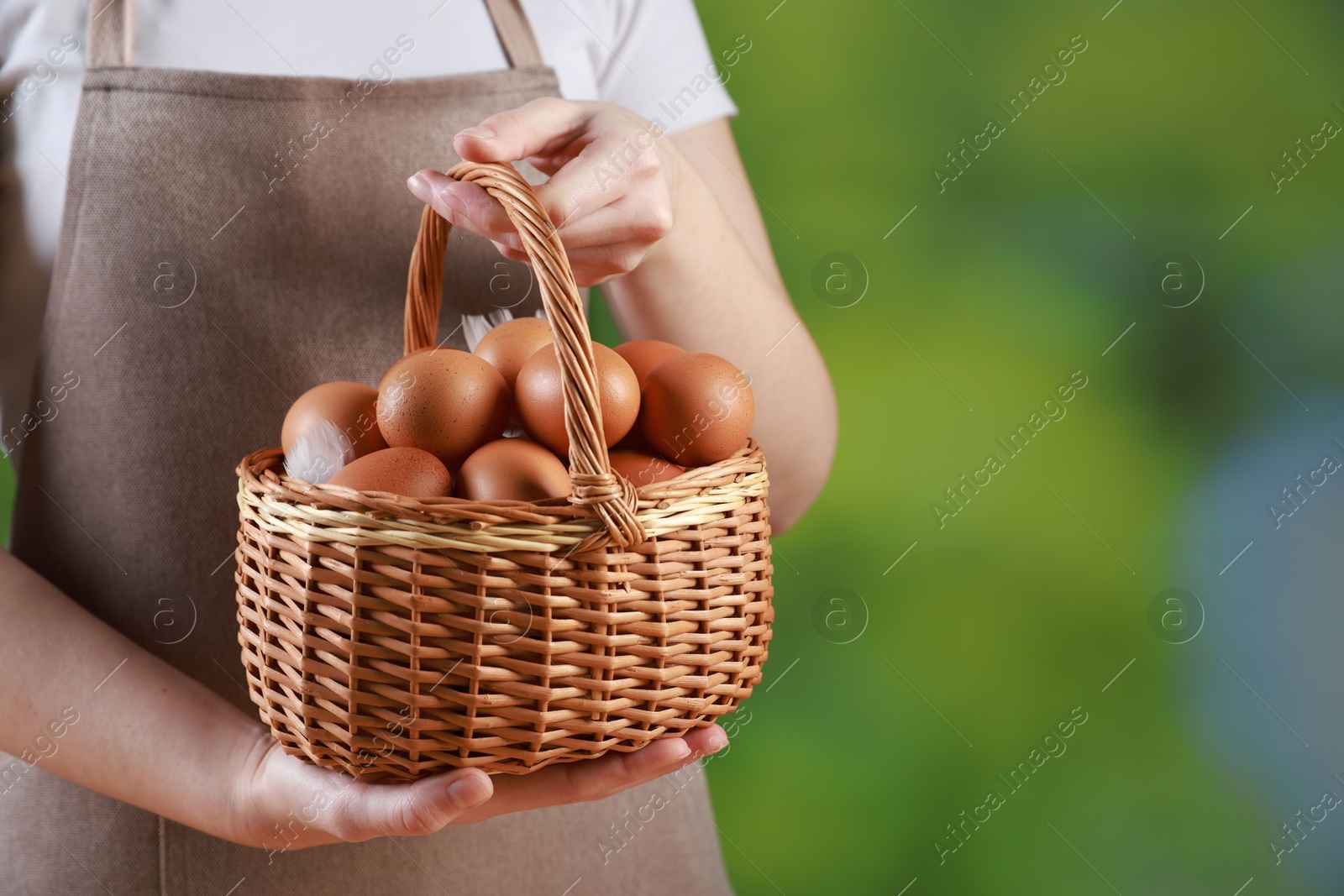 Photo of Woman with basket of eggs on blurred background, closeup. Space for text