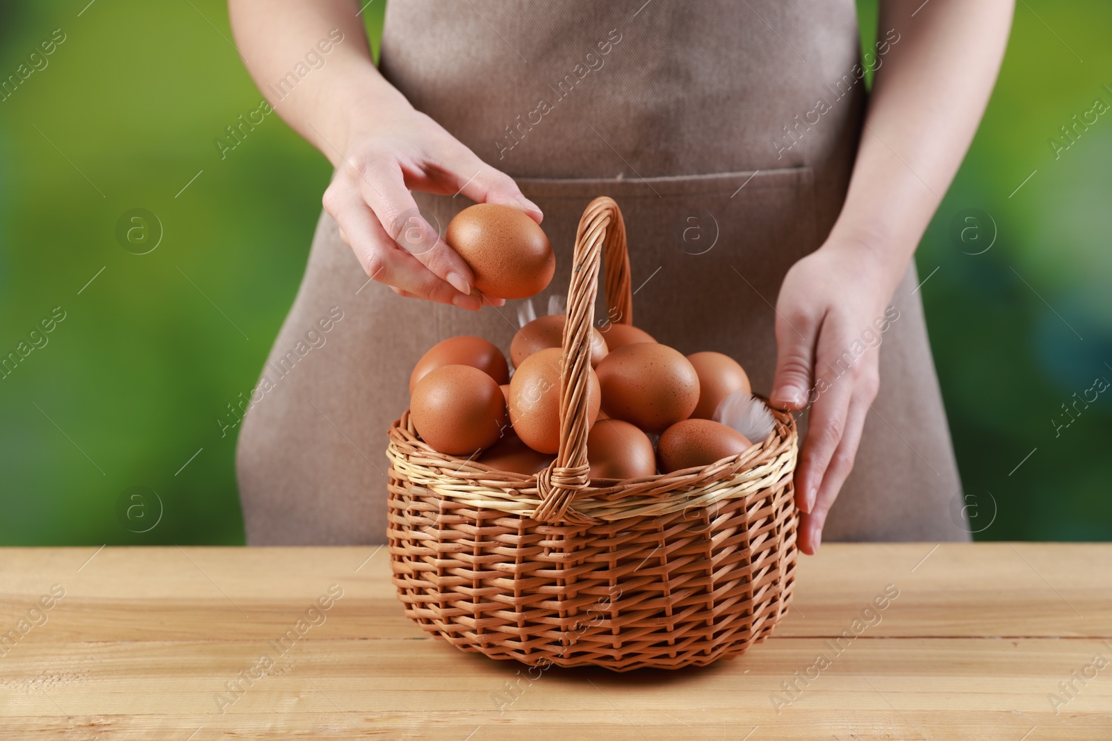 Photo of Woman with basket of eggs at wooden table on blurred background, closeup