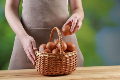 Photo of Woman with basket of eggs at wooden table on blurred background, closeup