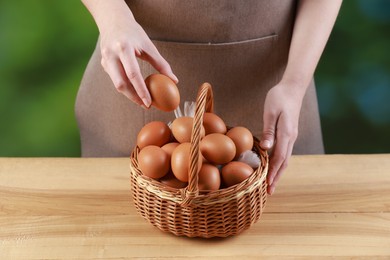 Photo of Woman with basket of eggs at wooden table on blurred background, closeup