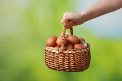 Photo of Woman with basket of eggs on blurred background, closeup. Space for text