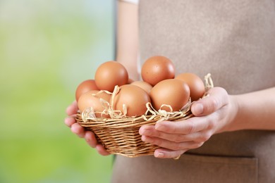 Photo of Woman with basket of eggs on blurred background, closeup. Space for text