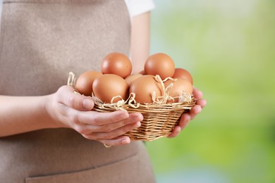 Photo of Woman with basket of eggs on blurred background, closeup