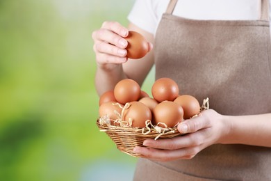 Photo of Woman with basket of eggs on blurred background, closeup. Space for text