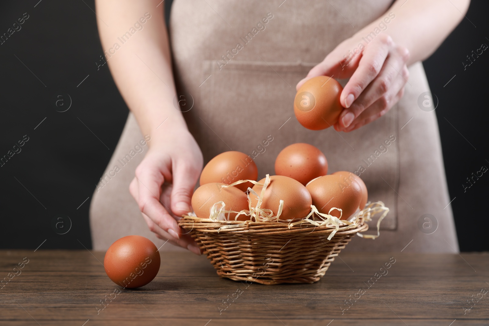 Photo of Woman with basket of eggs at wooden table on black background, closeup