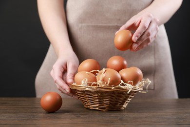 Photo of Woman with basket of eggs at wooden table on black background, closeup