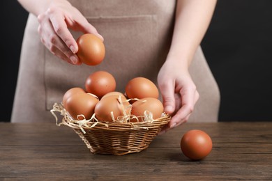 Photo of Woman with basket of eggs at wooden table on black background, closeup