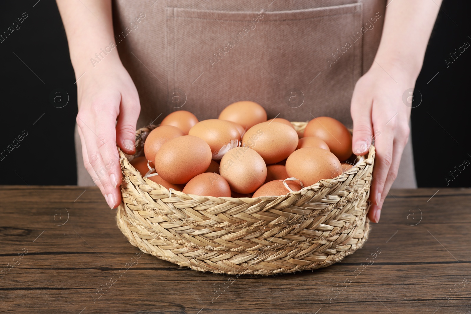 Photo of Woman with basket of eggs at wooden table on black background, closeup