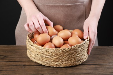 Photo of Woman with basket of eggs at wooden table on black background, closeup