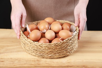 Photo of Woman with basket of eggs at wooden table on black background, closeup