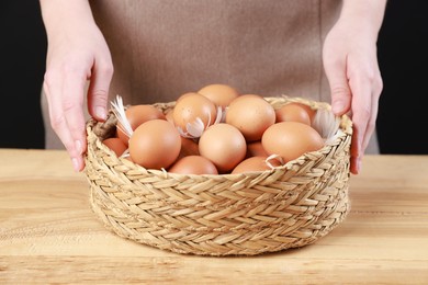 Photo of Woman with basket of eggs at wooden table on black background, closeup