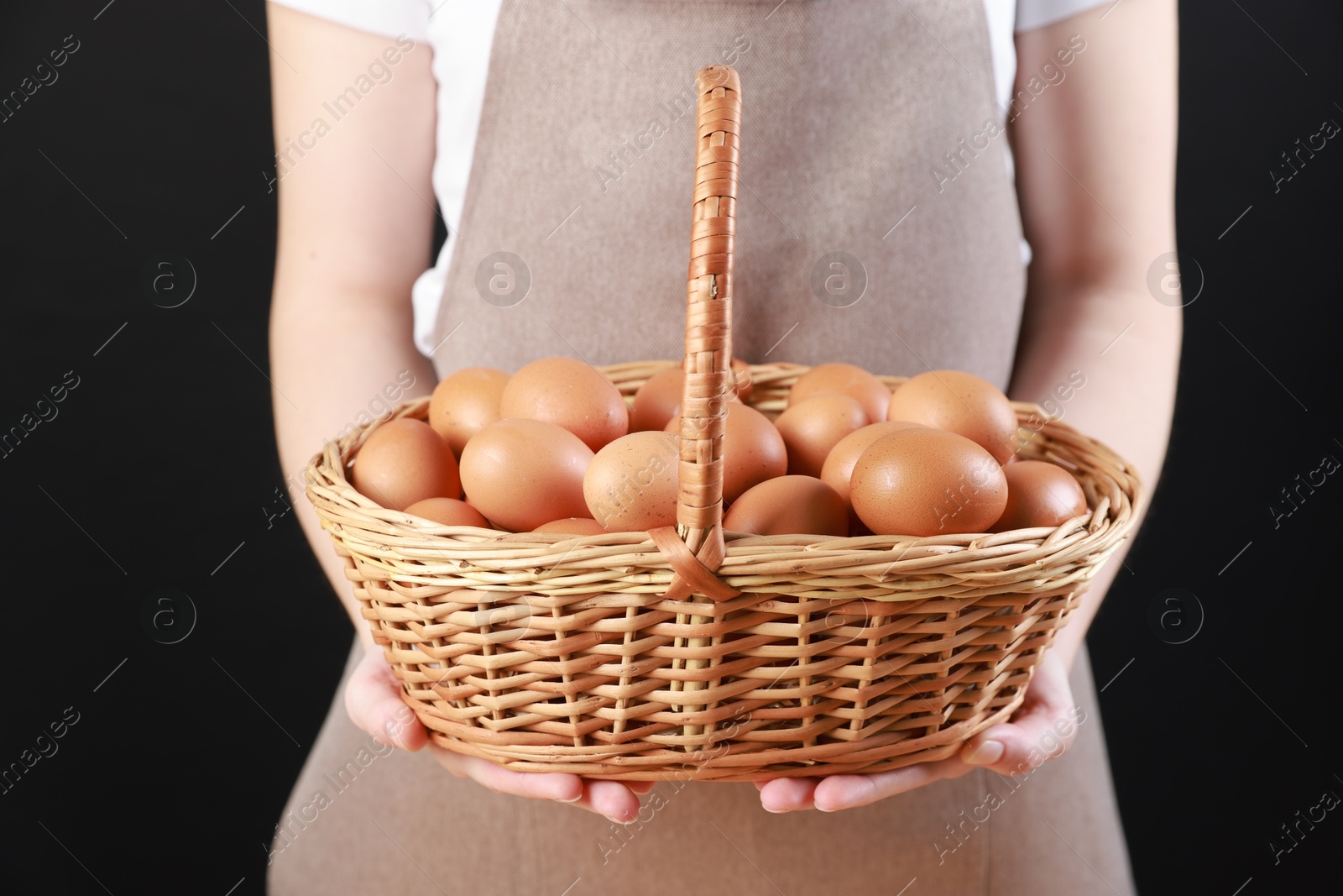 Photo of Woman with basket of eggs on black background, closeup