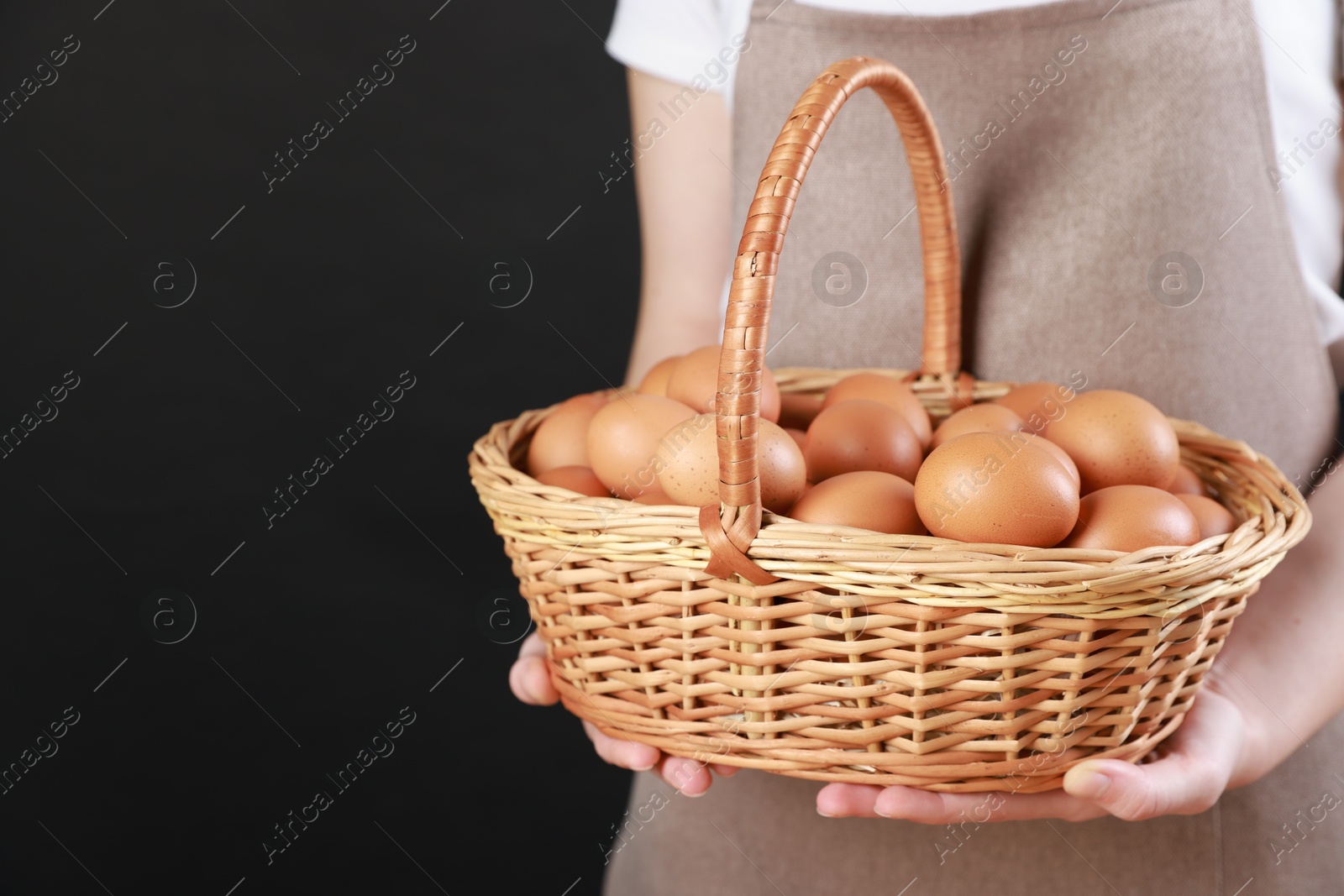 Photo of Woman with basket of eggs on black background, closeup. Space for text