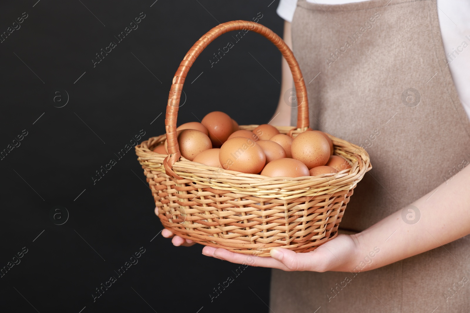 Photo of Woman with basket of eggs on black background, closeup. Space for text