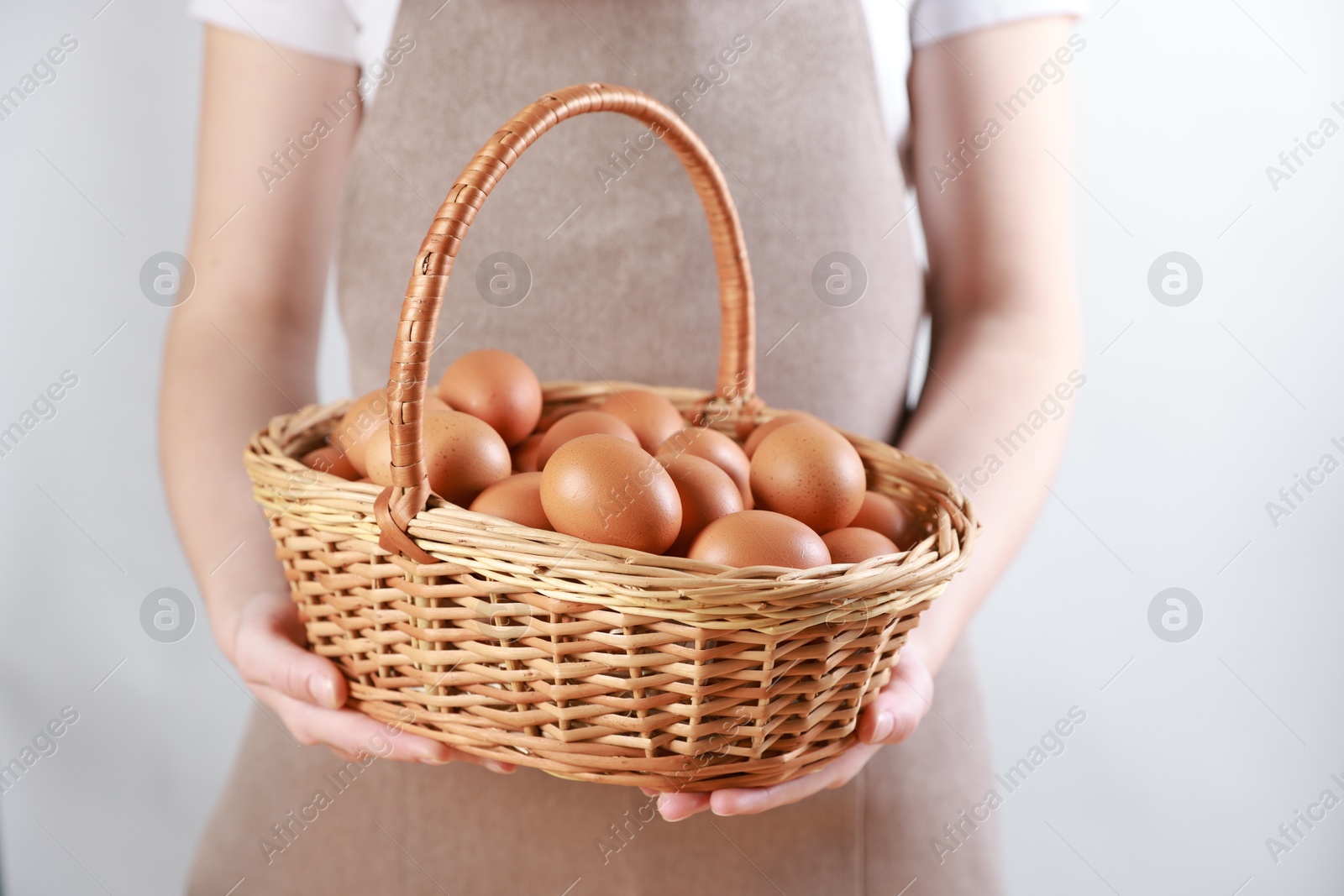 Photo of Woman with basket of eggs on light background, closeup