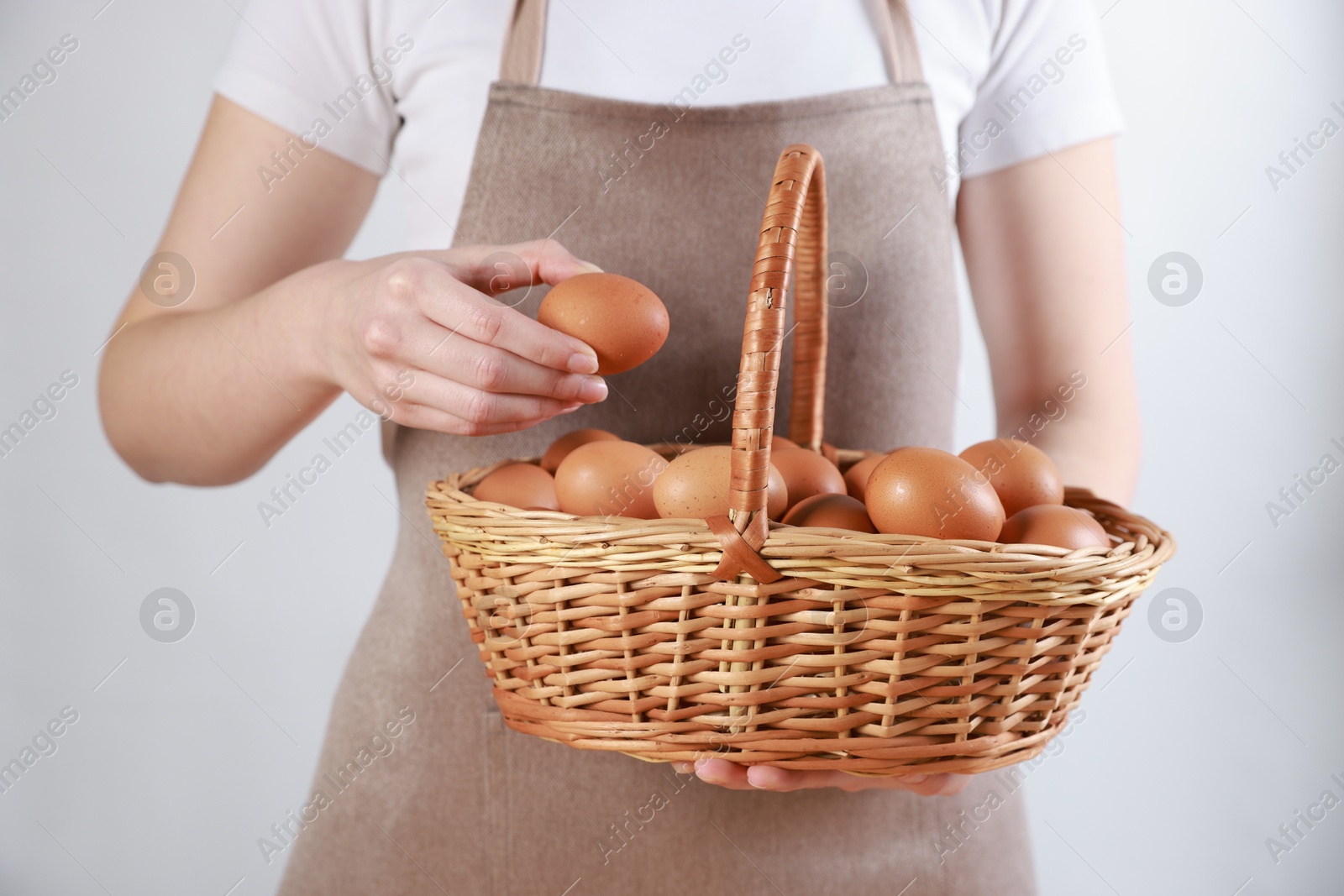 Photo of Woman with basket of eggs on light background, closeup