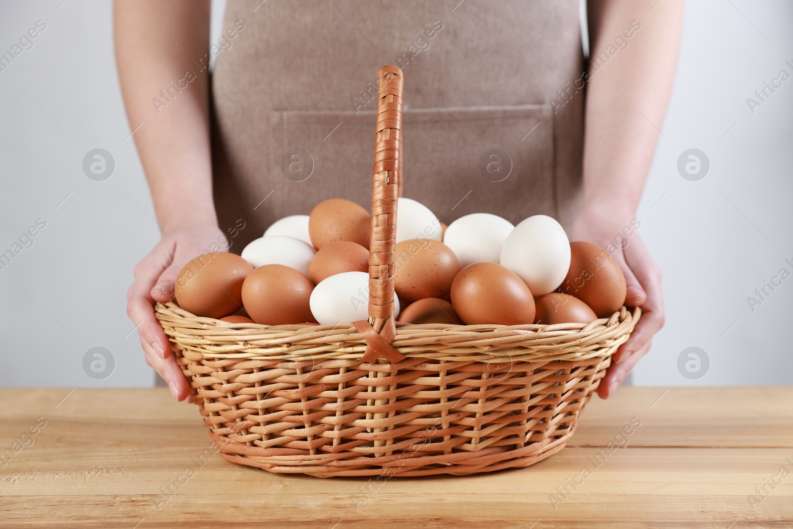 Photo of Woman with basket of eggs at wooden table on light background, closeup