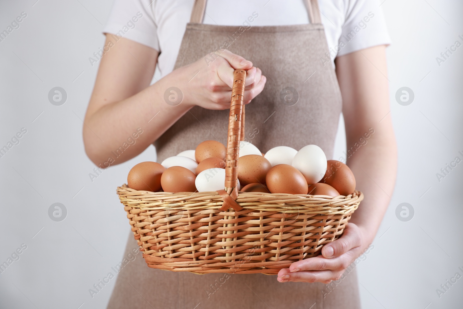 Photo of Woman with basket of eggs on light background, closeup