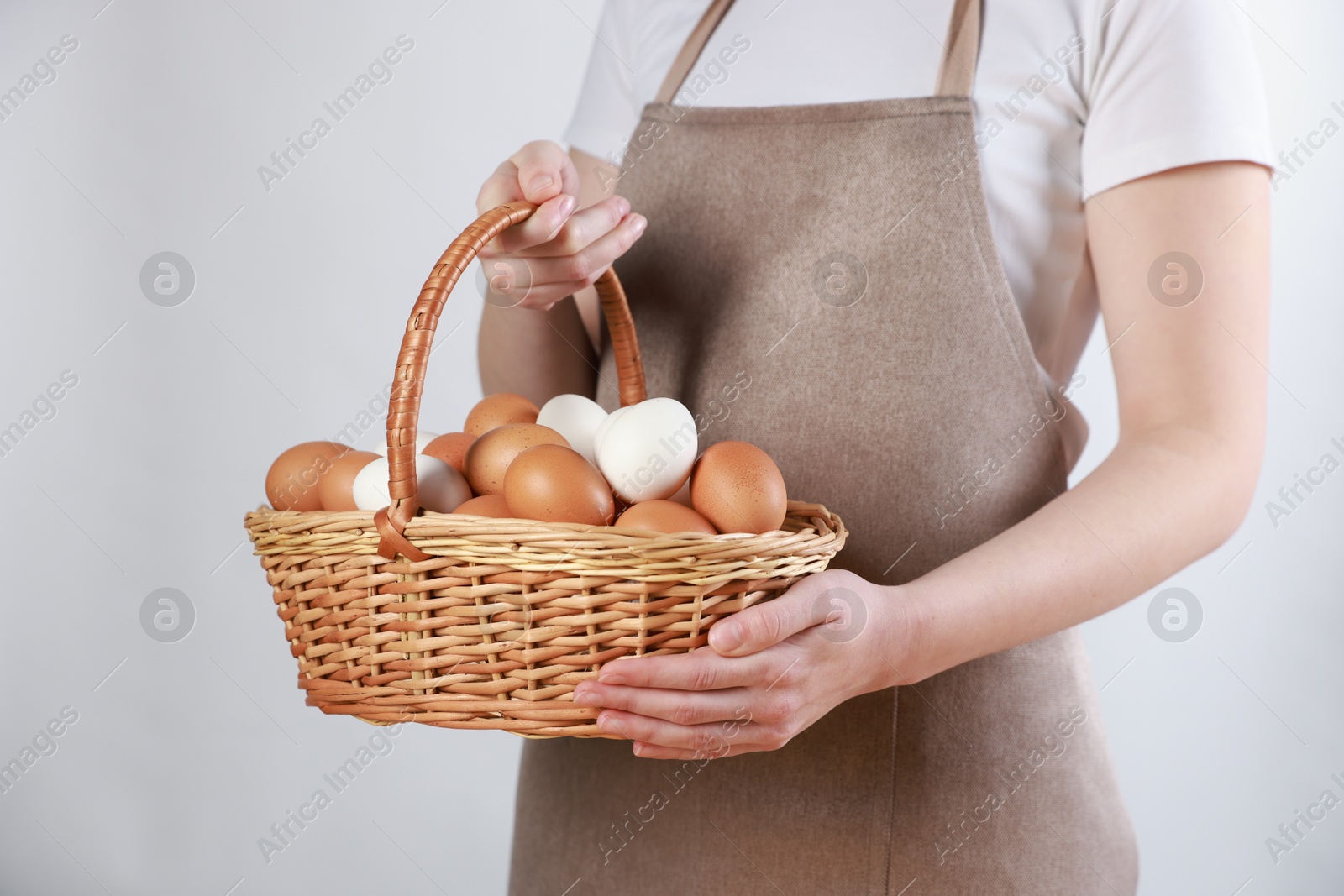 Photo of Woman with basket of eggs on light background, closeup