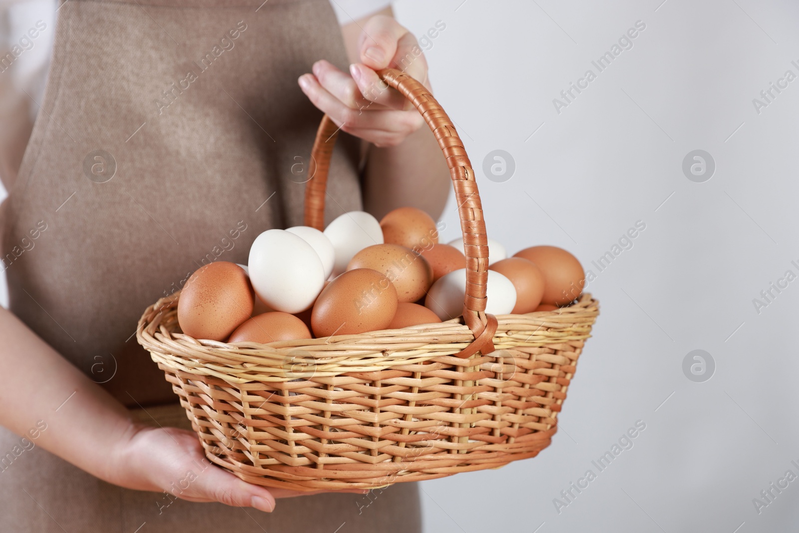 Photo of Woman with basket of eggs on light background, closeup. Space for text