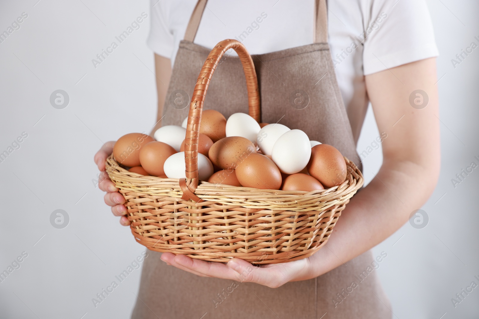 Photo of Woman with basket of eggs on light background, closeup