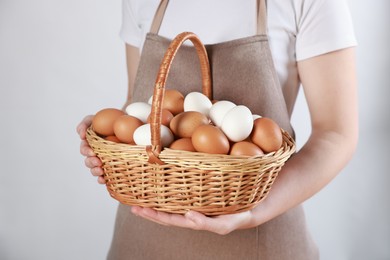 Photo of Woman with basket of eggs on light background, closeup