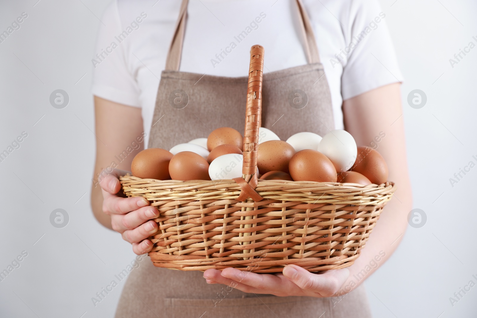 Photo of Woman with basket of eggs on light background, closeup