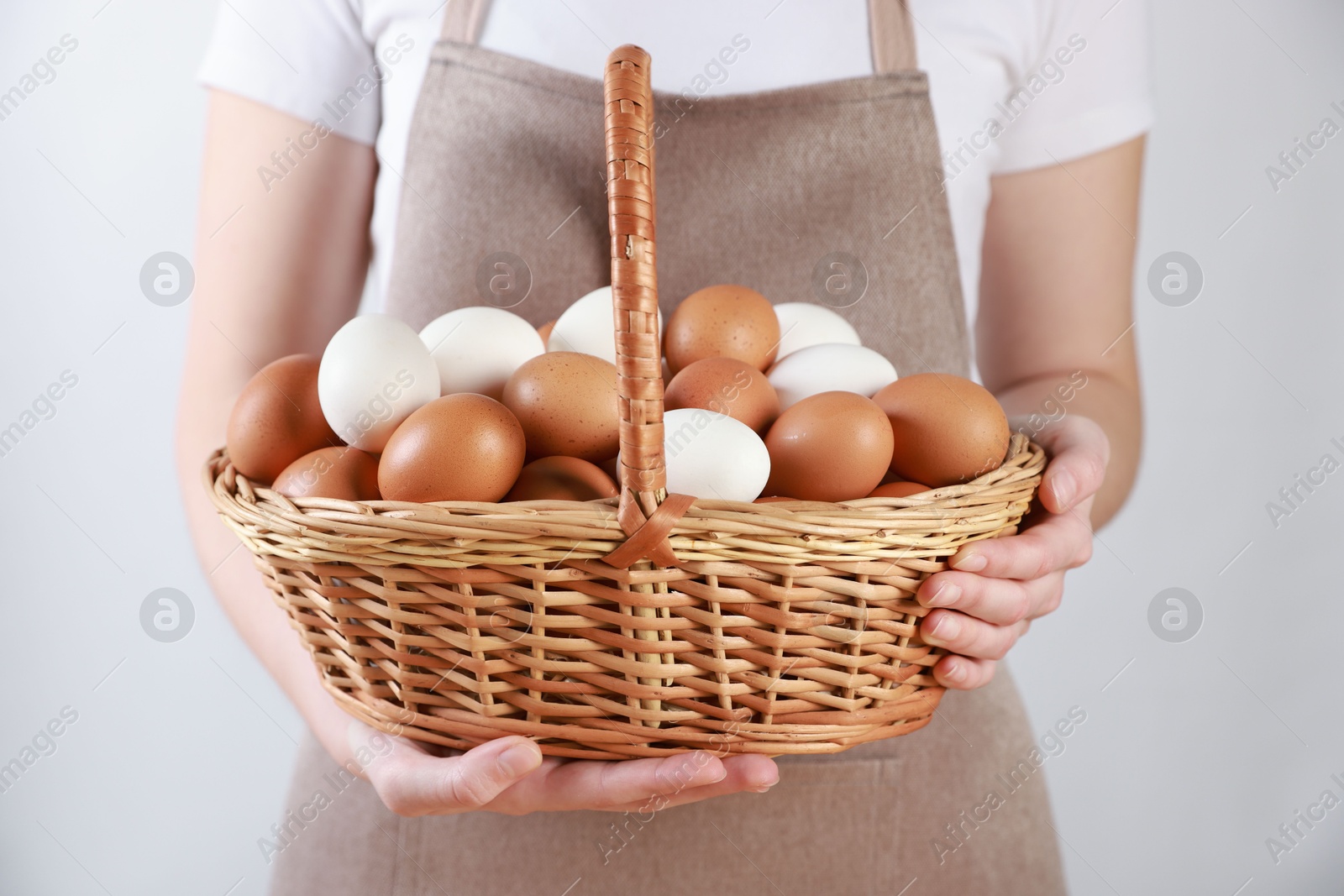 Photo of Woman with basket of eggs on light background, closeup