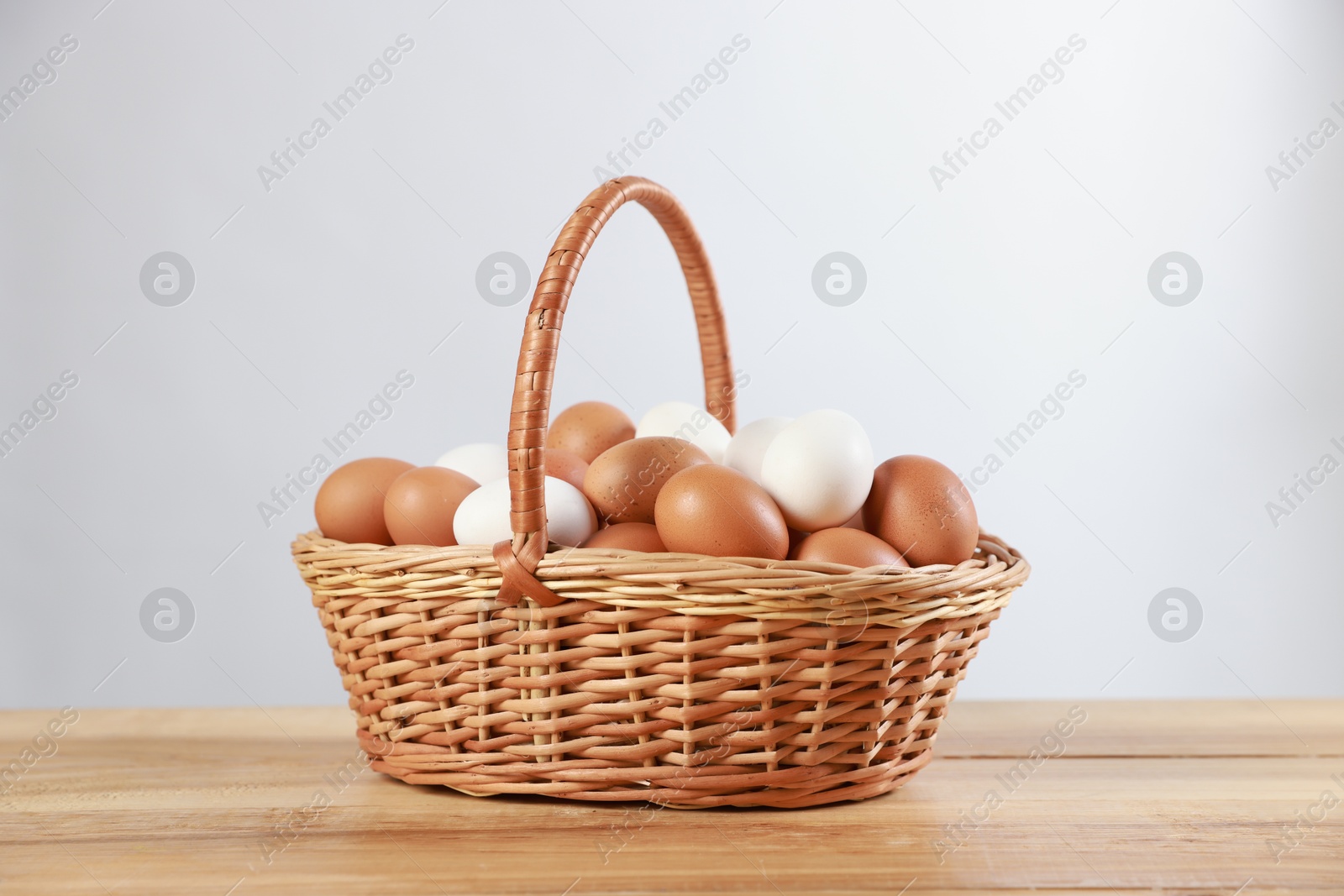 Photo of Many raw eggs in basket on wooden table