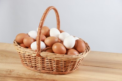 Photo of Many raw eggs in basket on wooden table