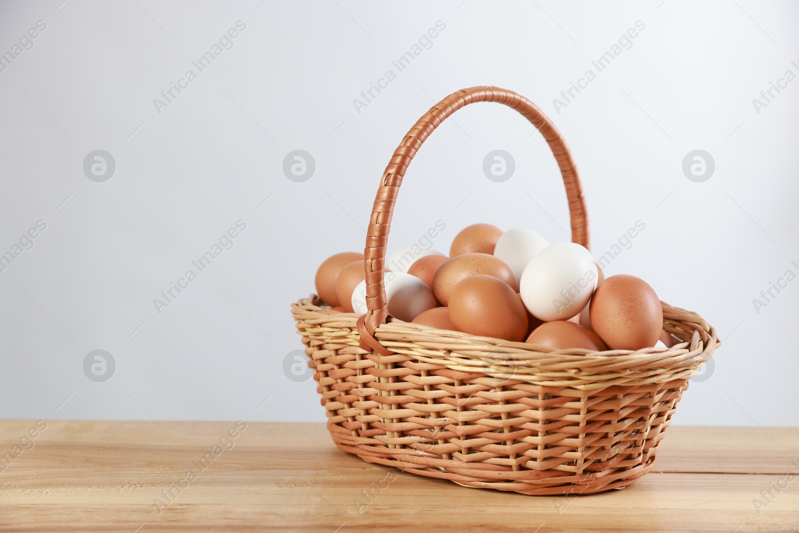 Photo of Many raw eggs in basket on wooden table. Space for text