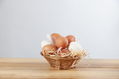 Photo of Many raw eggs in basket on wooden table. Space for text