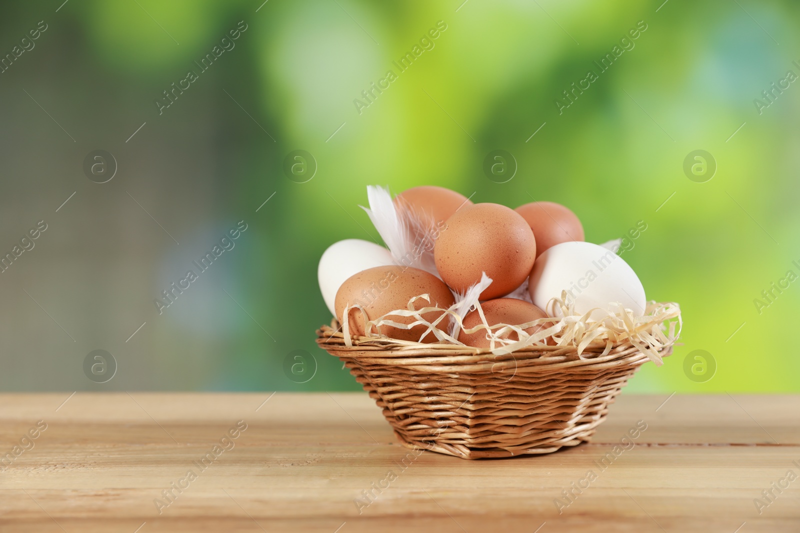 Photo of Many raw eggs in basket on wooden table, closeup. Space for text\