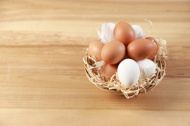 Photo of Many raw eggs in basket on wooden table, closeup. Space for text\