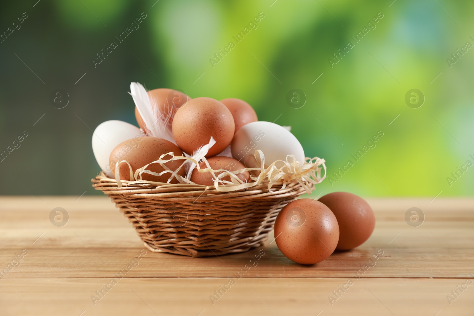 Photo of Many raw eggs in basket on wooden table, closeup