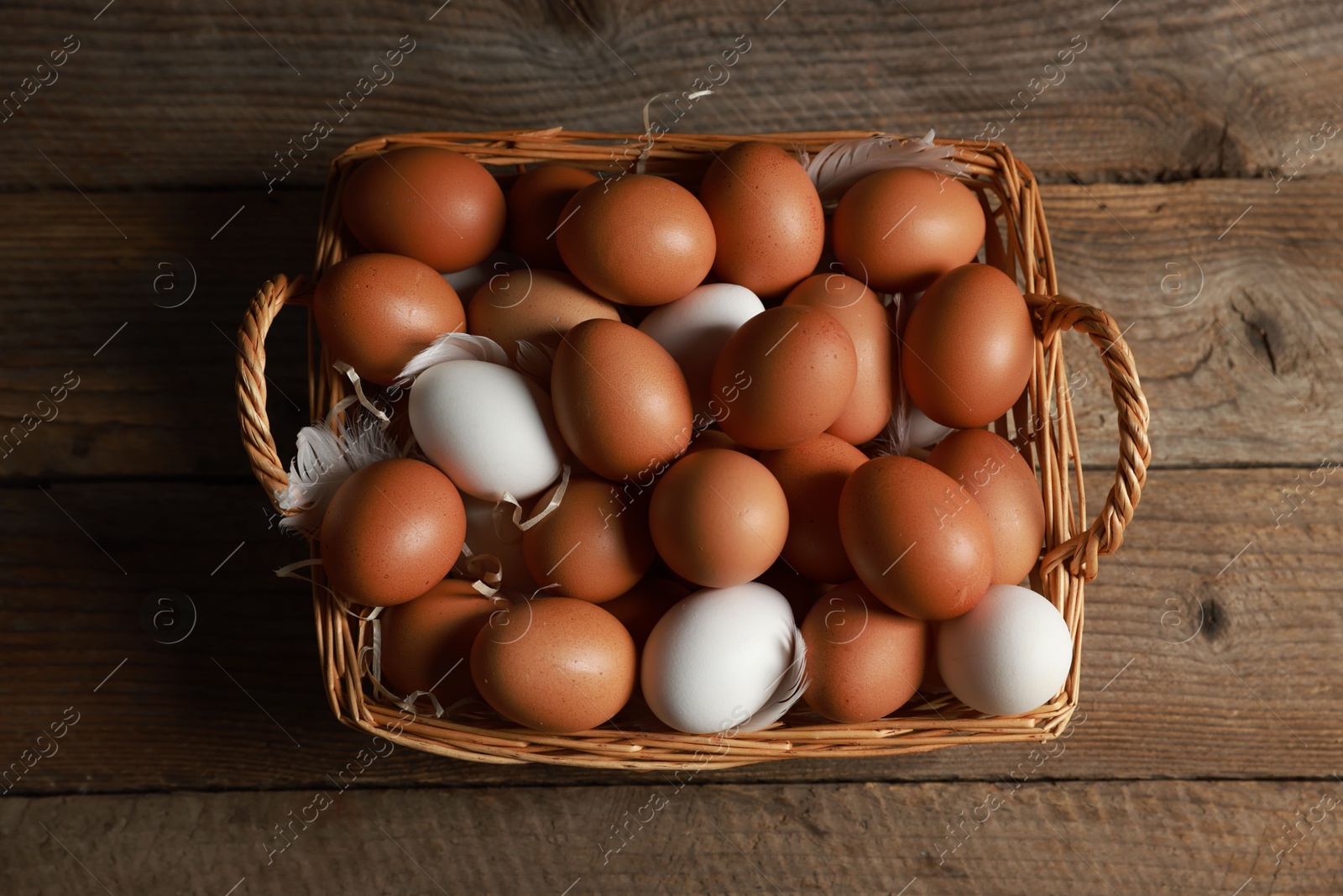 Photo of Many raw eggs in basket on wooden table, above view