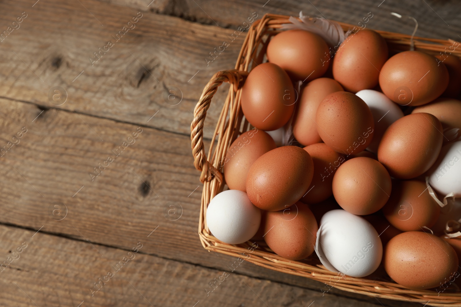 Photo of Many raw eggs in basket on wooden table, above view. Space for text