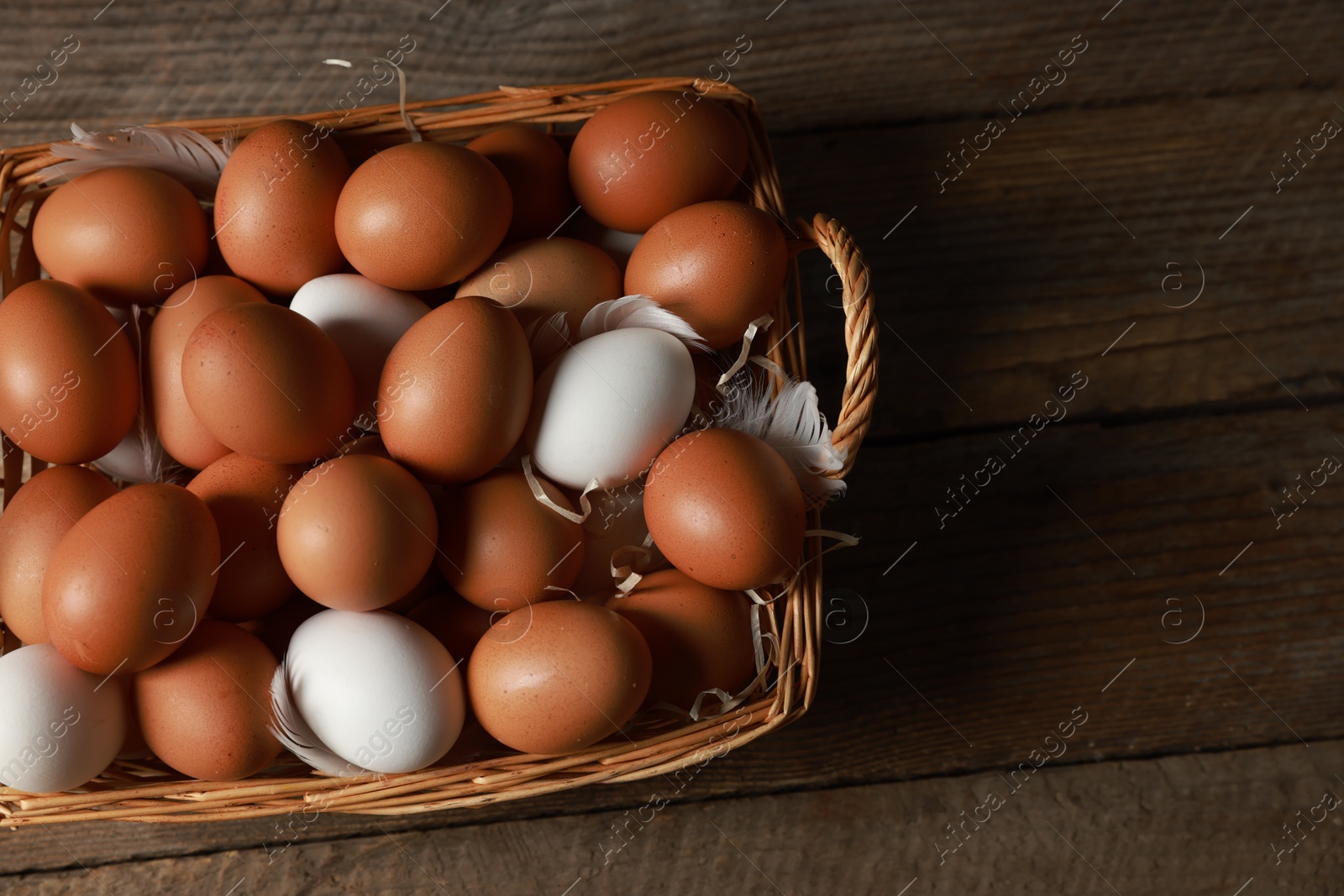 Photo of Many raw eggs in basket on wooden table, above view