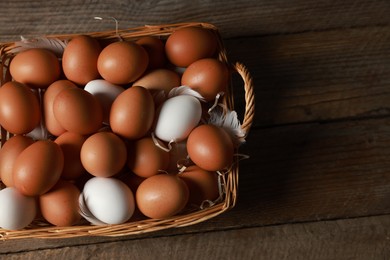 Photo of Many raw eggs in basket on wooden table, above view