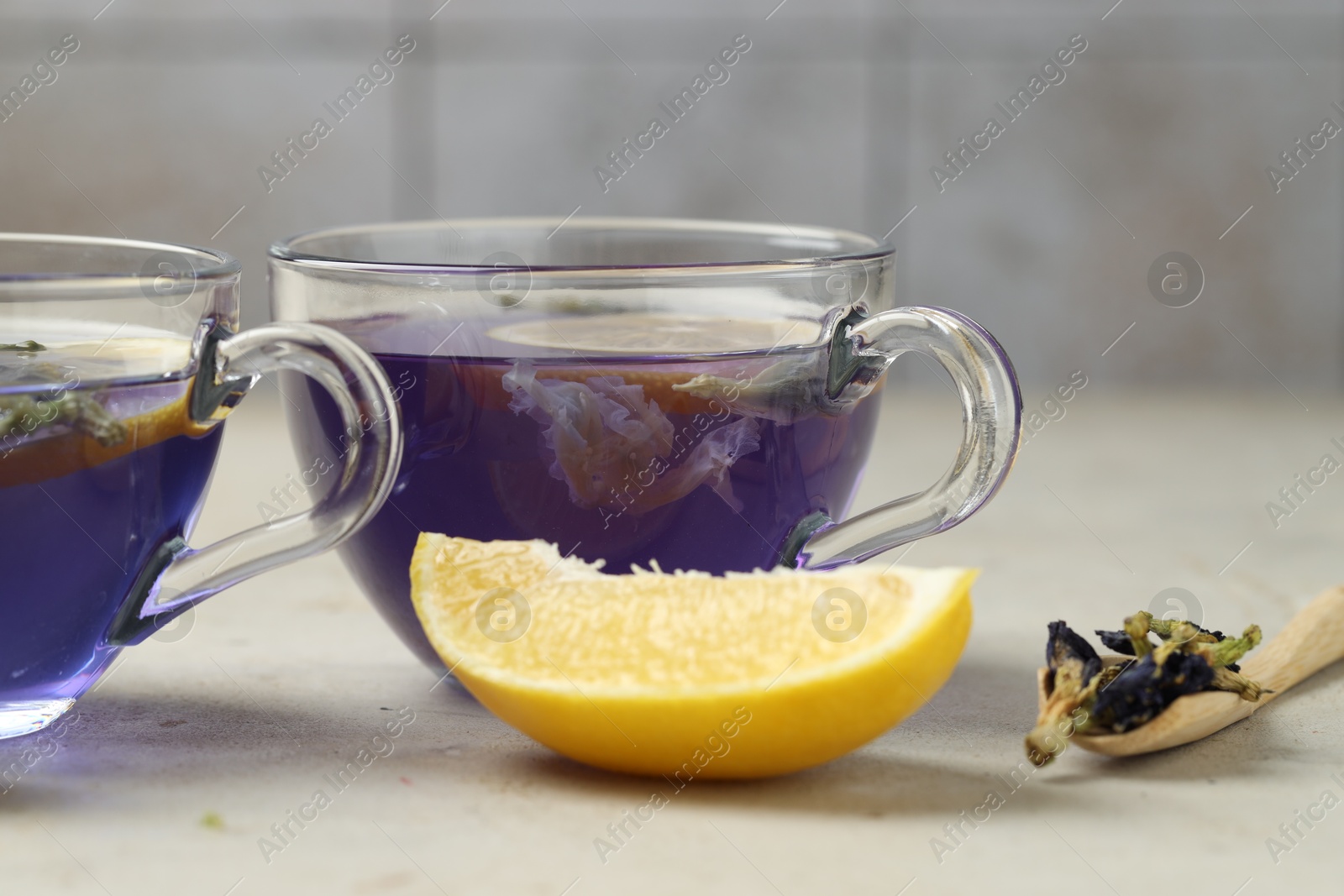 Photo of Delicious butterfly pea flower tea with lemon on gray textured table, closeup