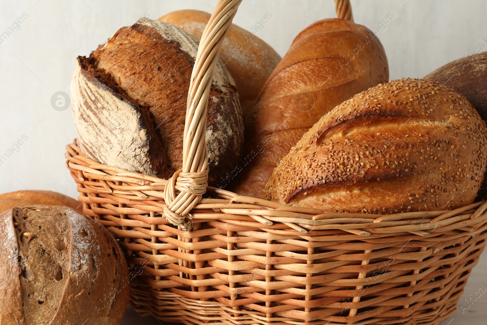 Photo of Different freshly baked breads in wicker basket on table, closeup